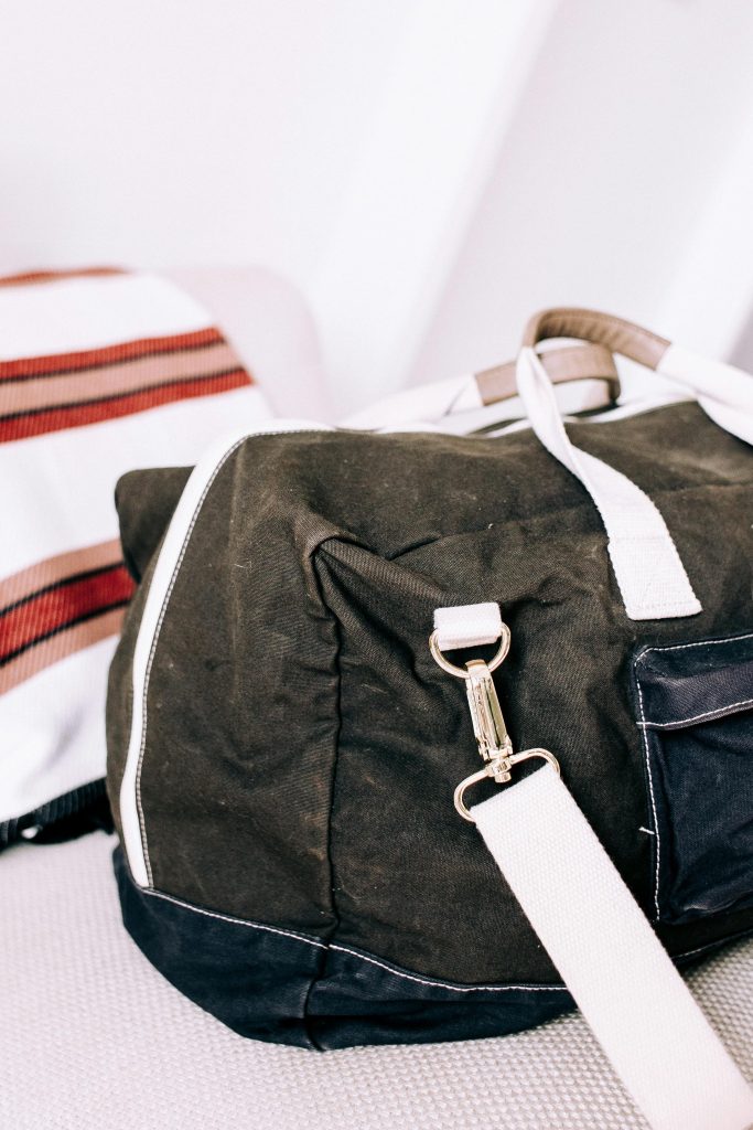 A black denim bag with white straps and silver metal snap hook is placed on a sofa
