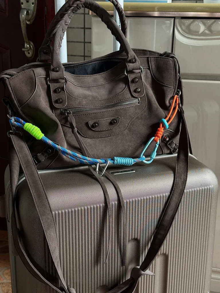 Blue and white rope with a green knot and hooks attached to the bag on top of a suitcase