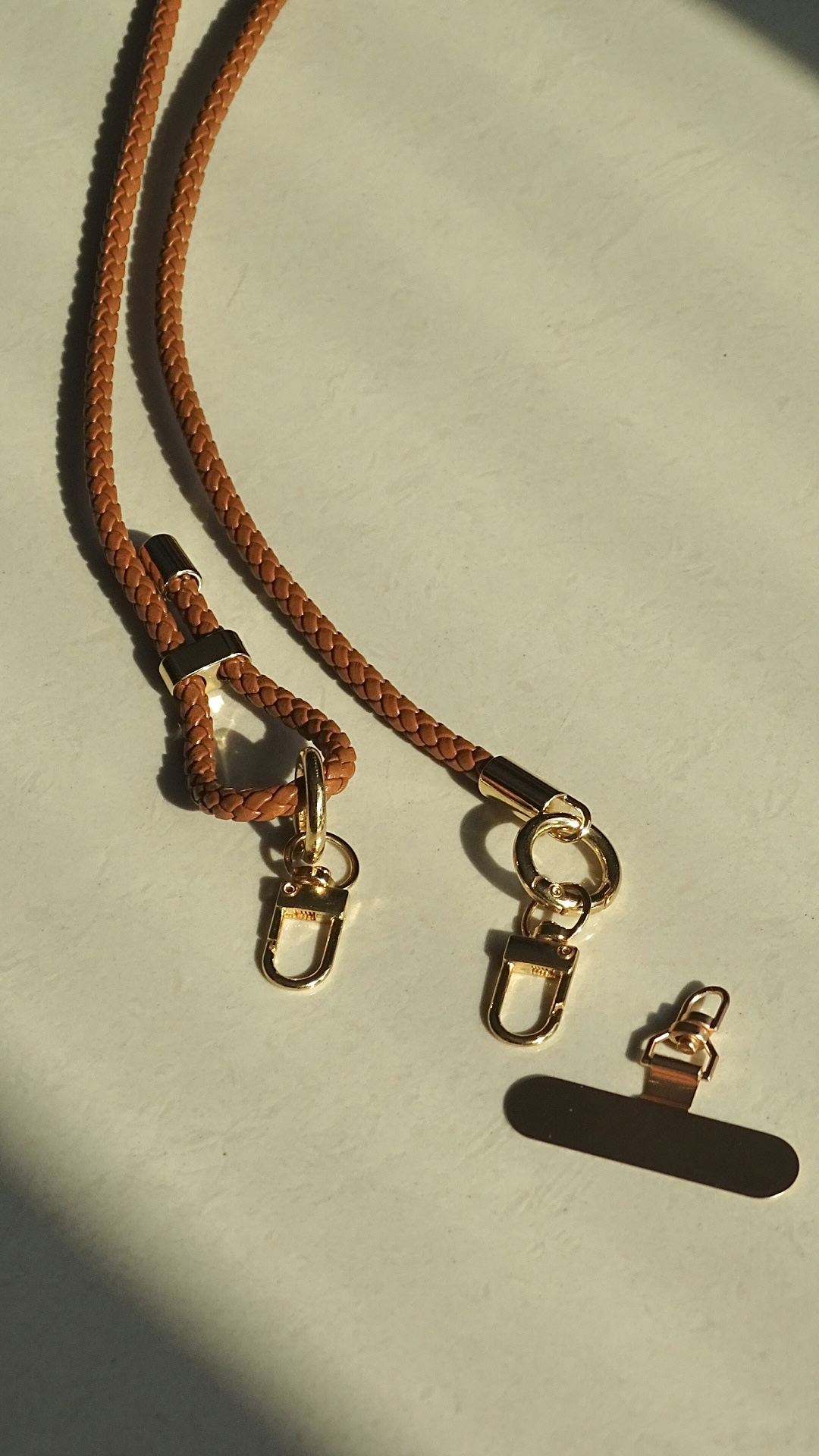 Leather phone strap with golden metal hardware on a beige surface